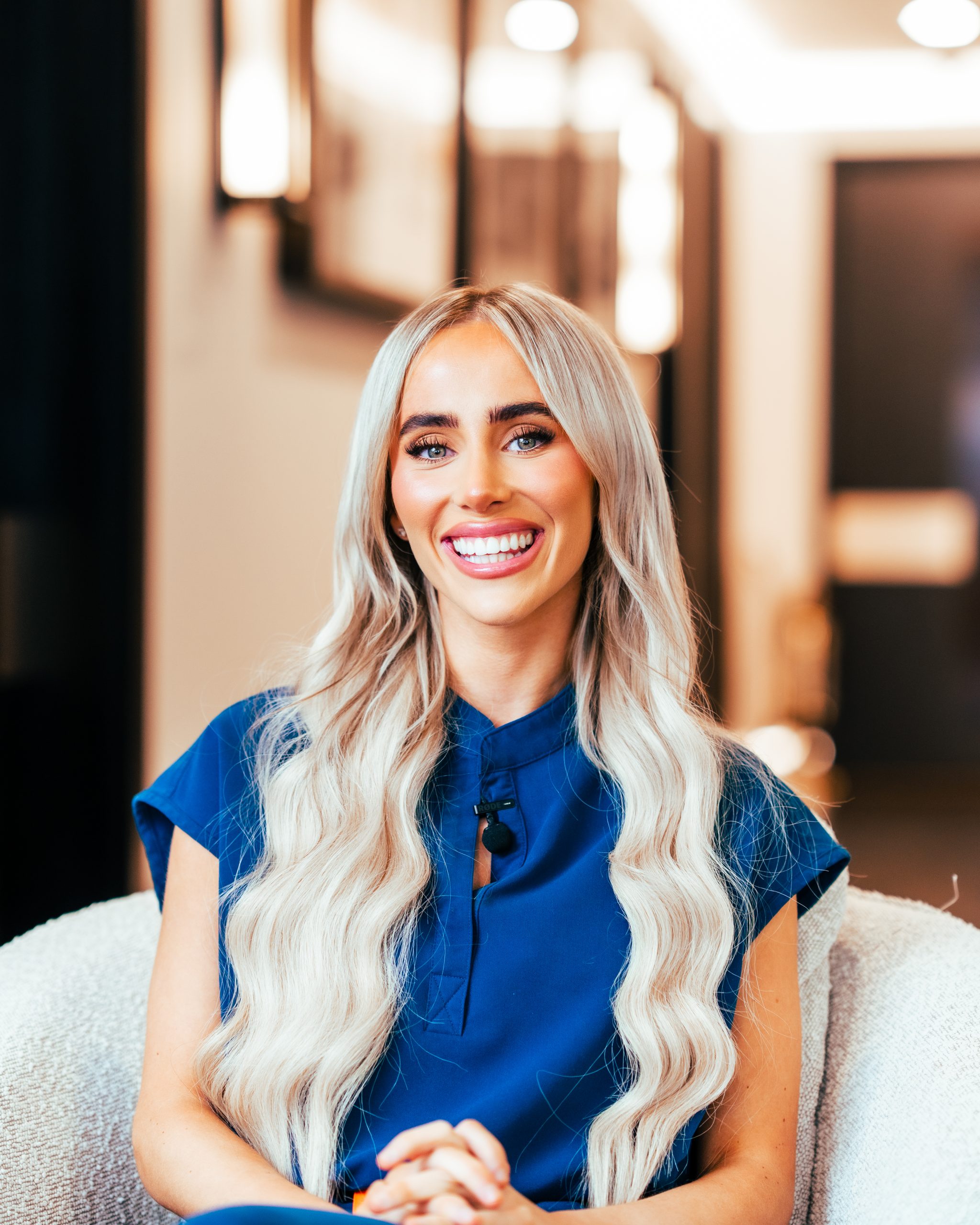 Dental Nurse Jess Brookes smiling in her deep blue scrubs while sat on a comfy white chair